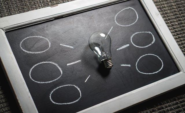A light bulb surrounded by empty balloons on a small blackboard
