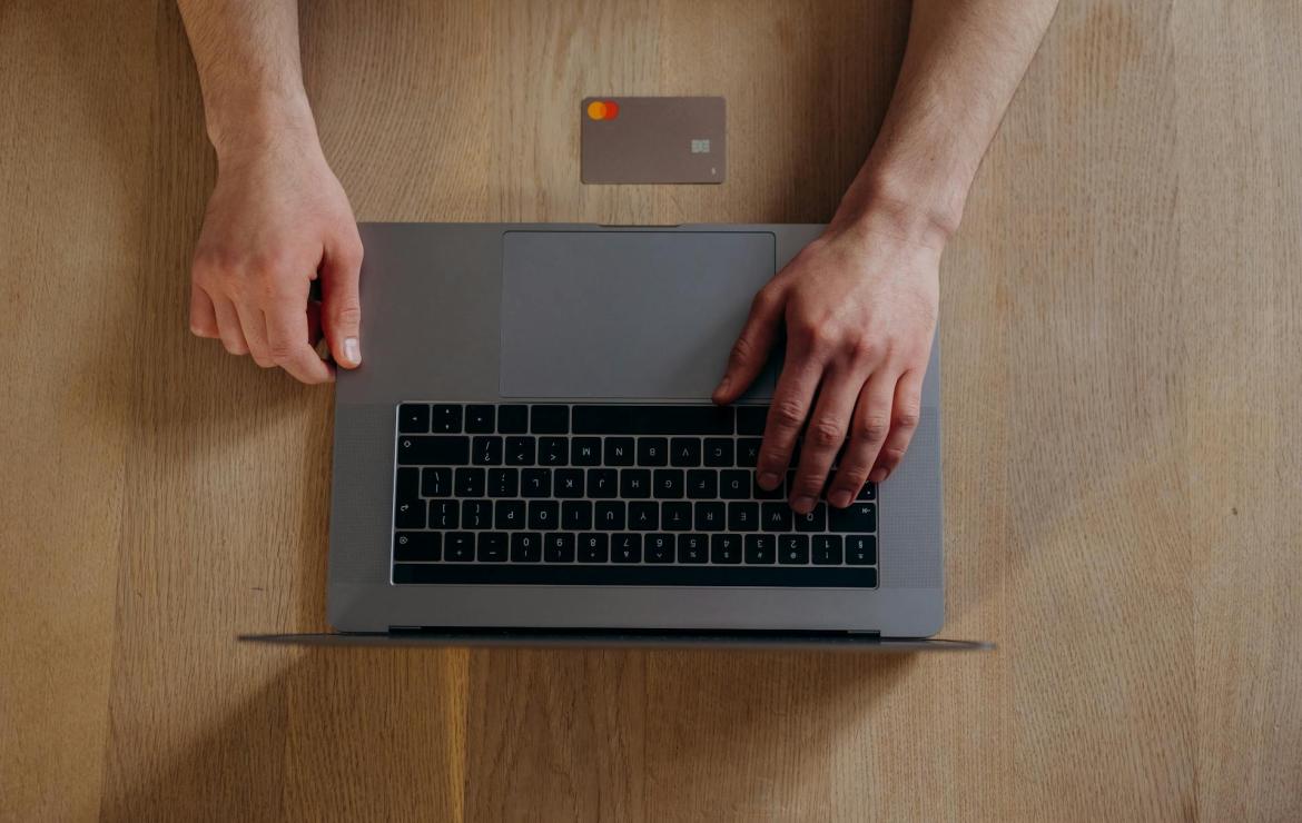 a Laptop from the top down, with hands using it, and a credit card on the table