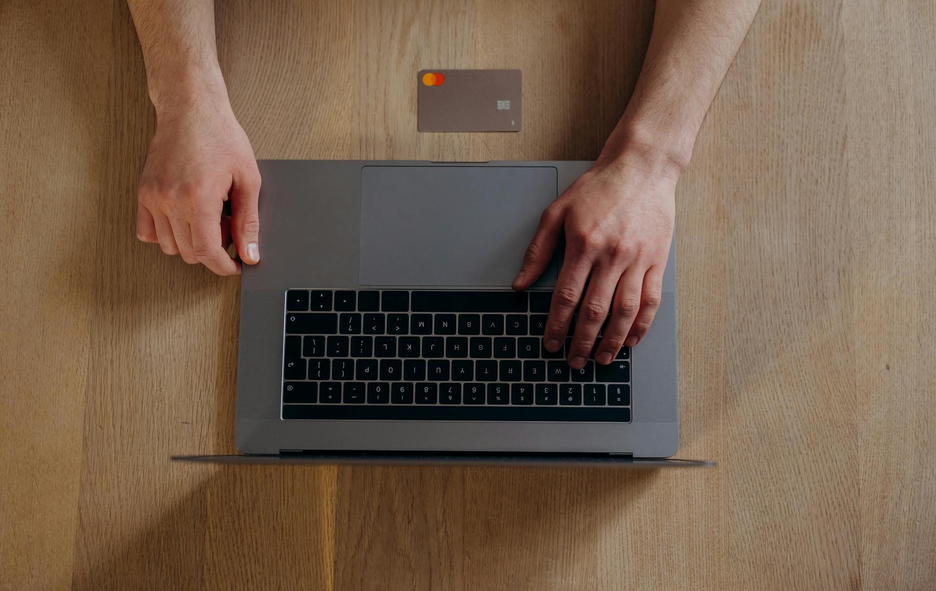 a Laptop from the top down, with hands using it, and a credit card on the table