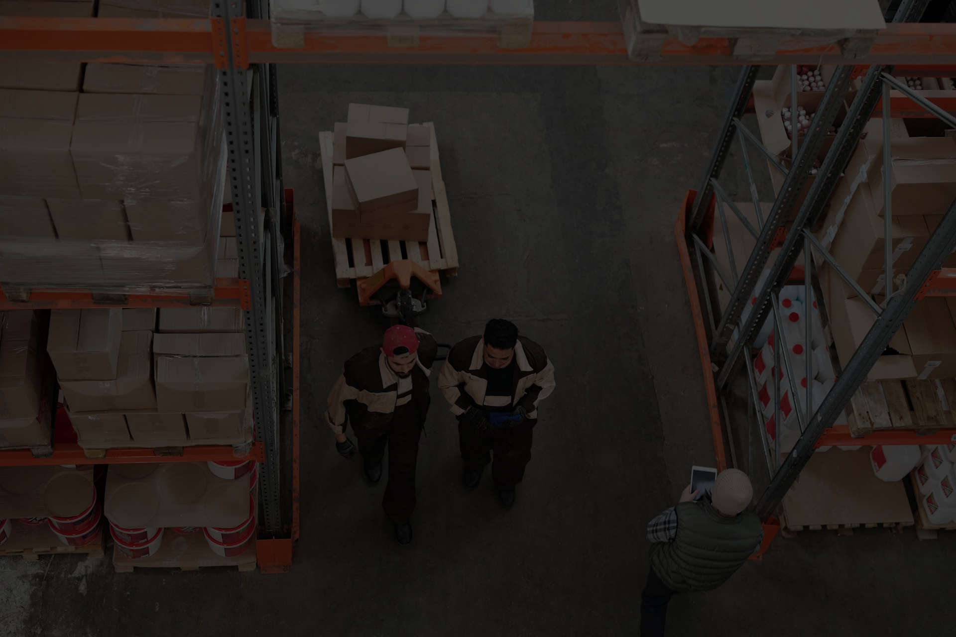 People walking in a warehouse, pulling boxes on a cart