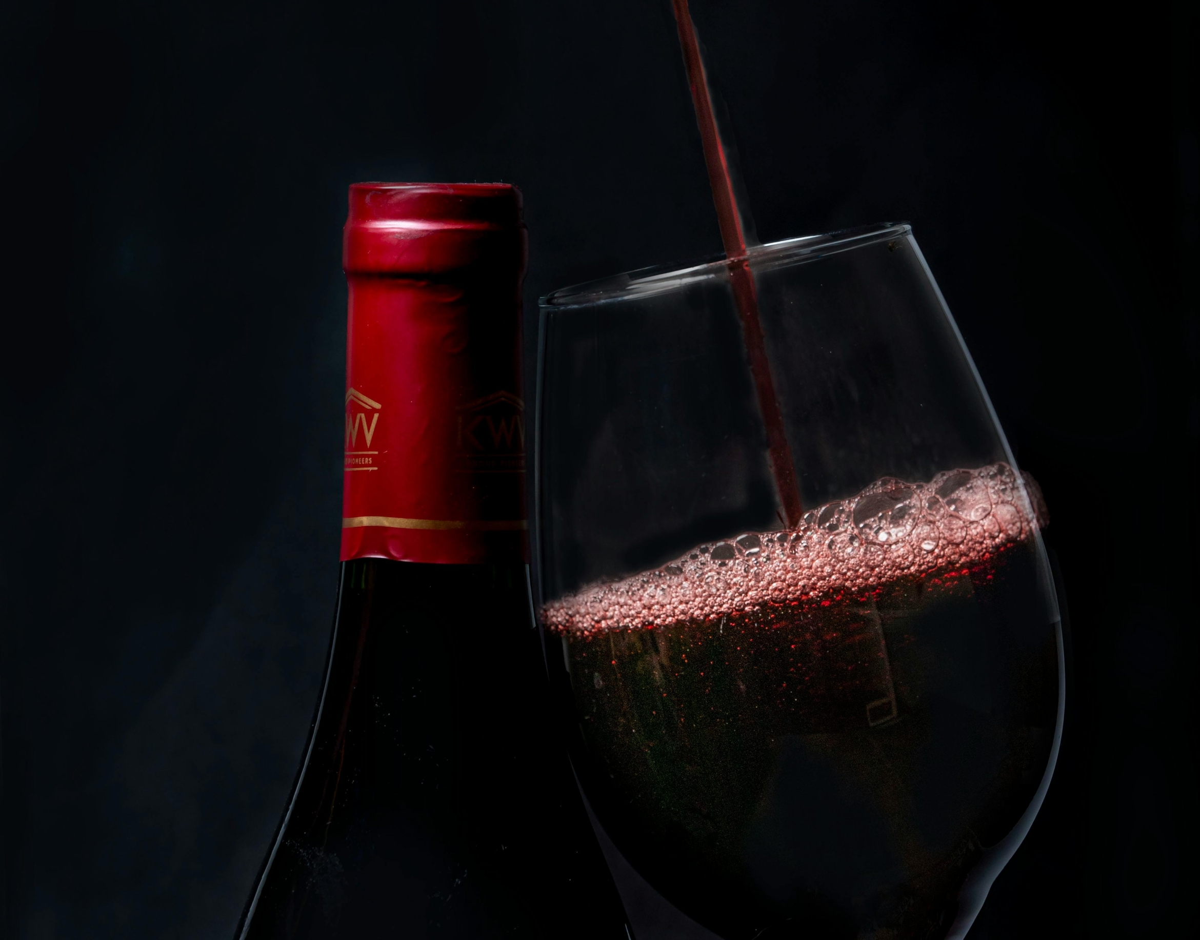 A wine bottle and class, with wine being poured into the glass.