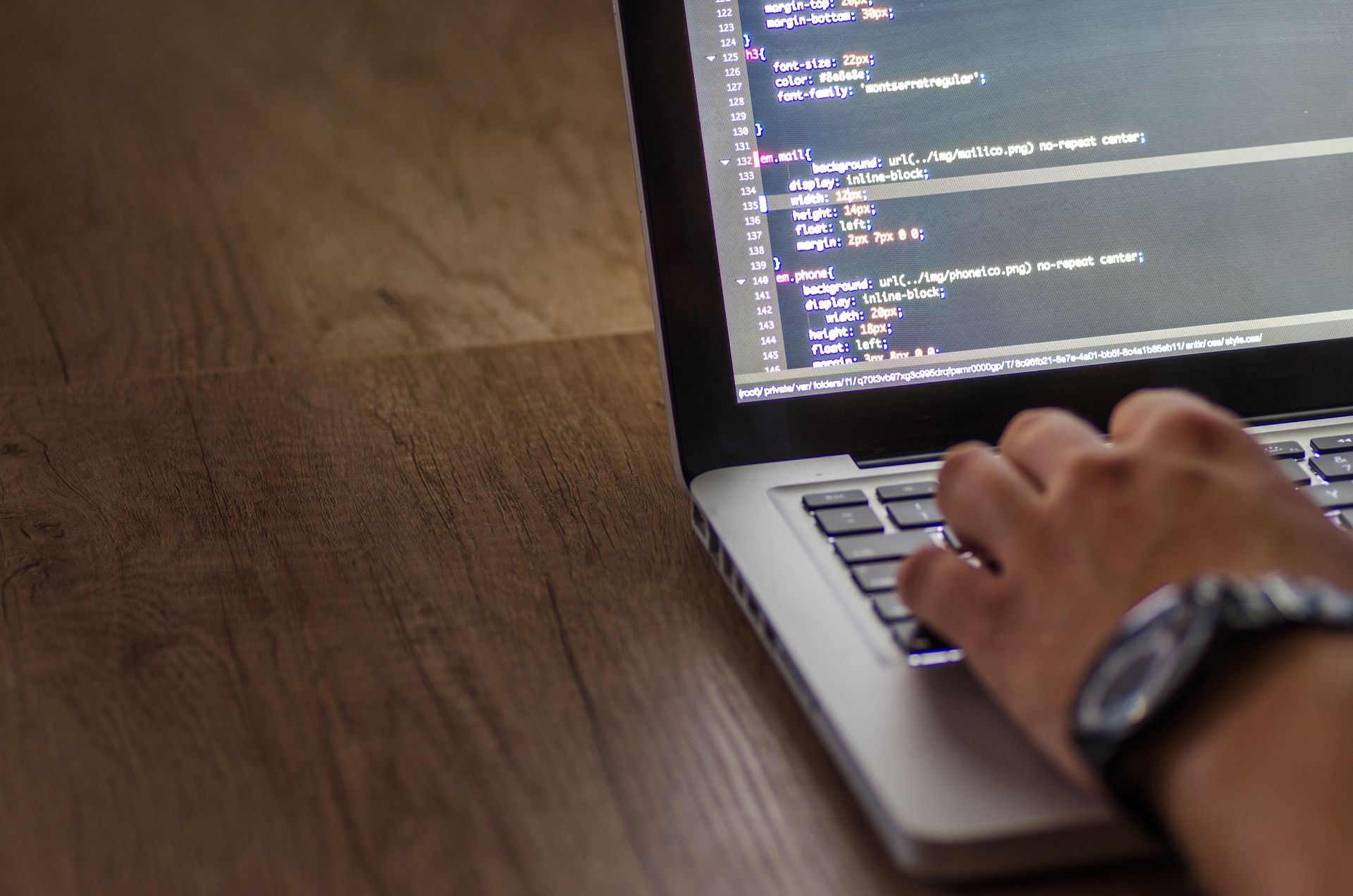 A hand on an open laptop with code on the screen.