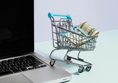 A shopping cart with money, on the edge of a laptop