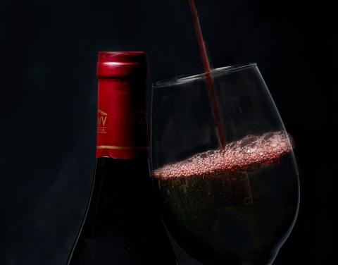 A wine bottle and class, with wine being poured into the glass.