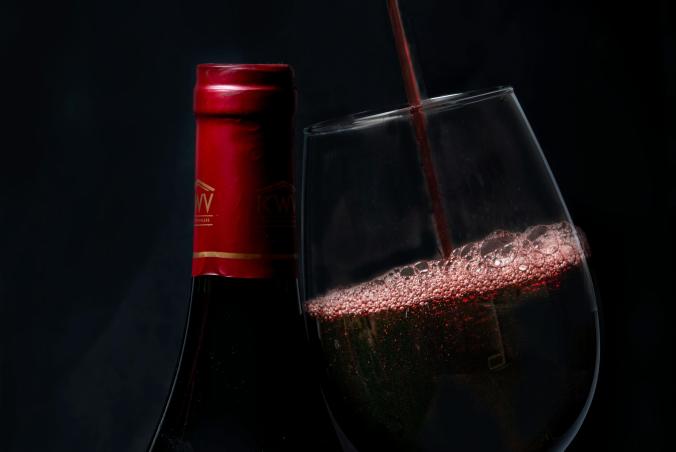 A wine bottle and class, with wine being poured into the glass.